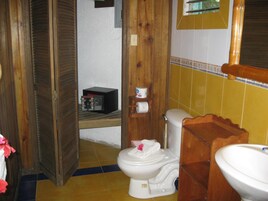 Un baño con inodoro, estante de madera con artículos de aseo y lavabo.
