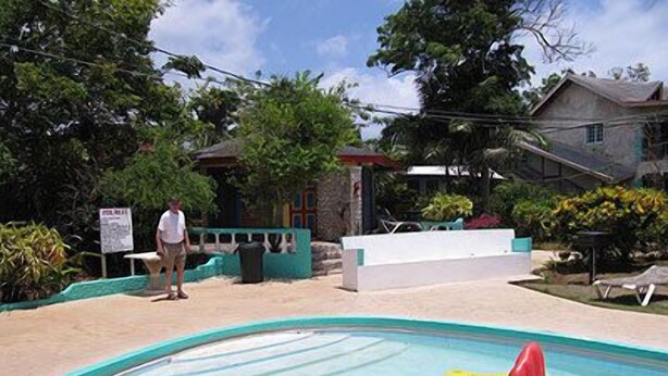 Una piscina con botes inflables, rodeada de un área ajardinada con árboles y un edificio al fondo.