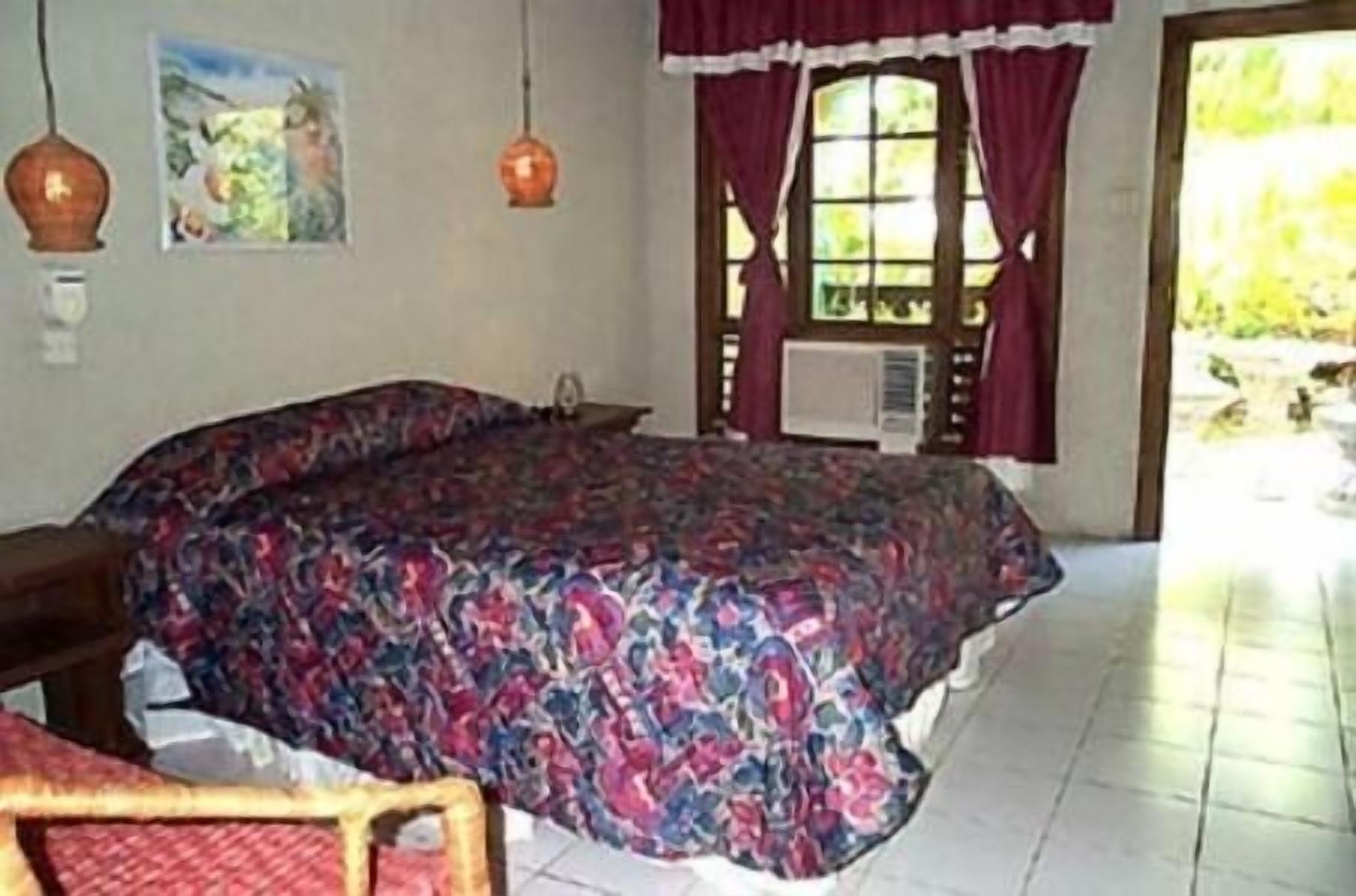 A bedroom with a large bed, a chair, a window with curtains, and a wall-mounted air conditioning unit.