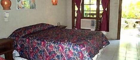 A bedroom with a large bed, a chair, a window with curtains, and a wall-mounted air conditioning unit.
