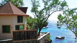 Una casa costera con base de piedra, balcón de madera y vista al mar.
