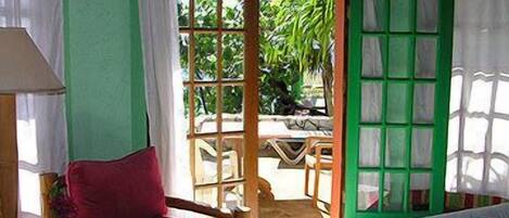 A room with a wooden chair, a bed, and a view of an outdoor area with a table and chairs.