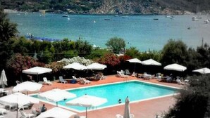 A pool area with lounge chairs and umbrellas, overlooking a body of water with boats. - Hotel Select (Campo nell'Elba)