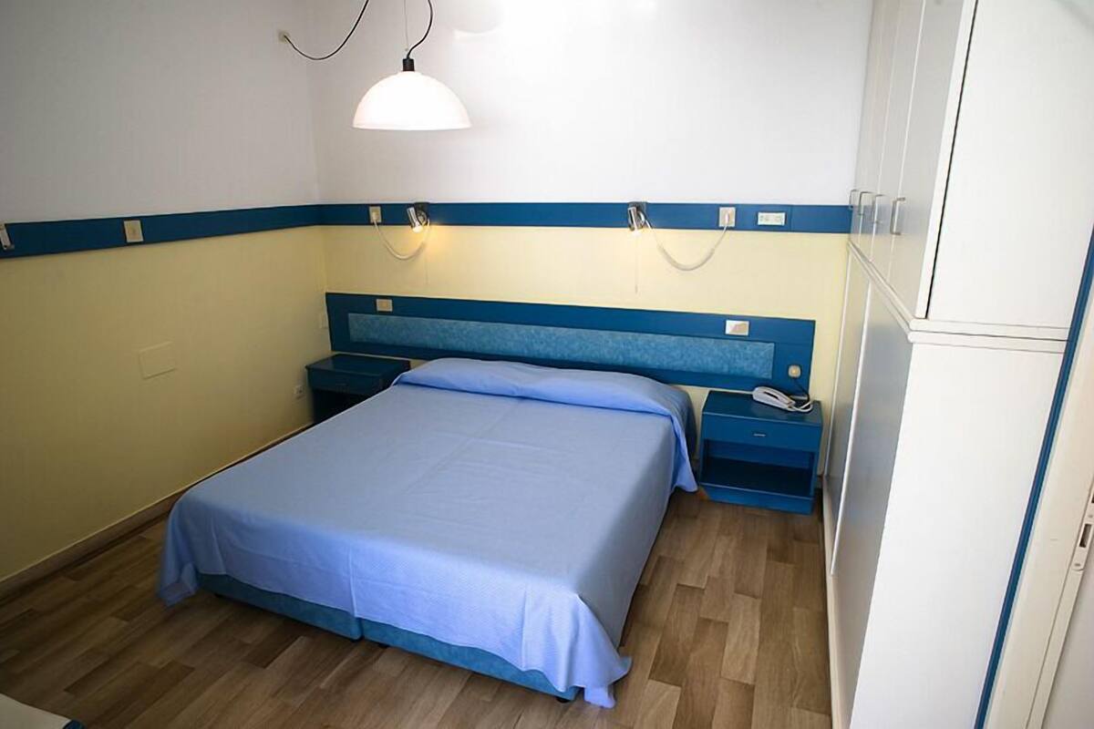 A bedroom with a single bed, bedside tables, a telephone, and a wall-mounted lamp.