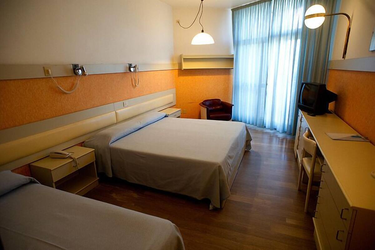 A hotel room with two beds, a desk, a chair, a television, and a window with curtains.