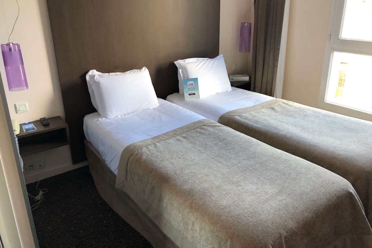 Une chambre d’hôtel avec deux lits, une table de chevet, une lampe et une fenêtre.