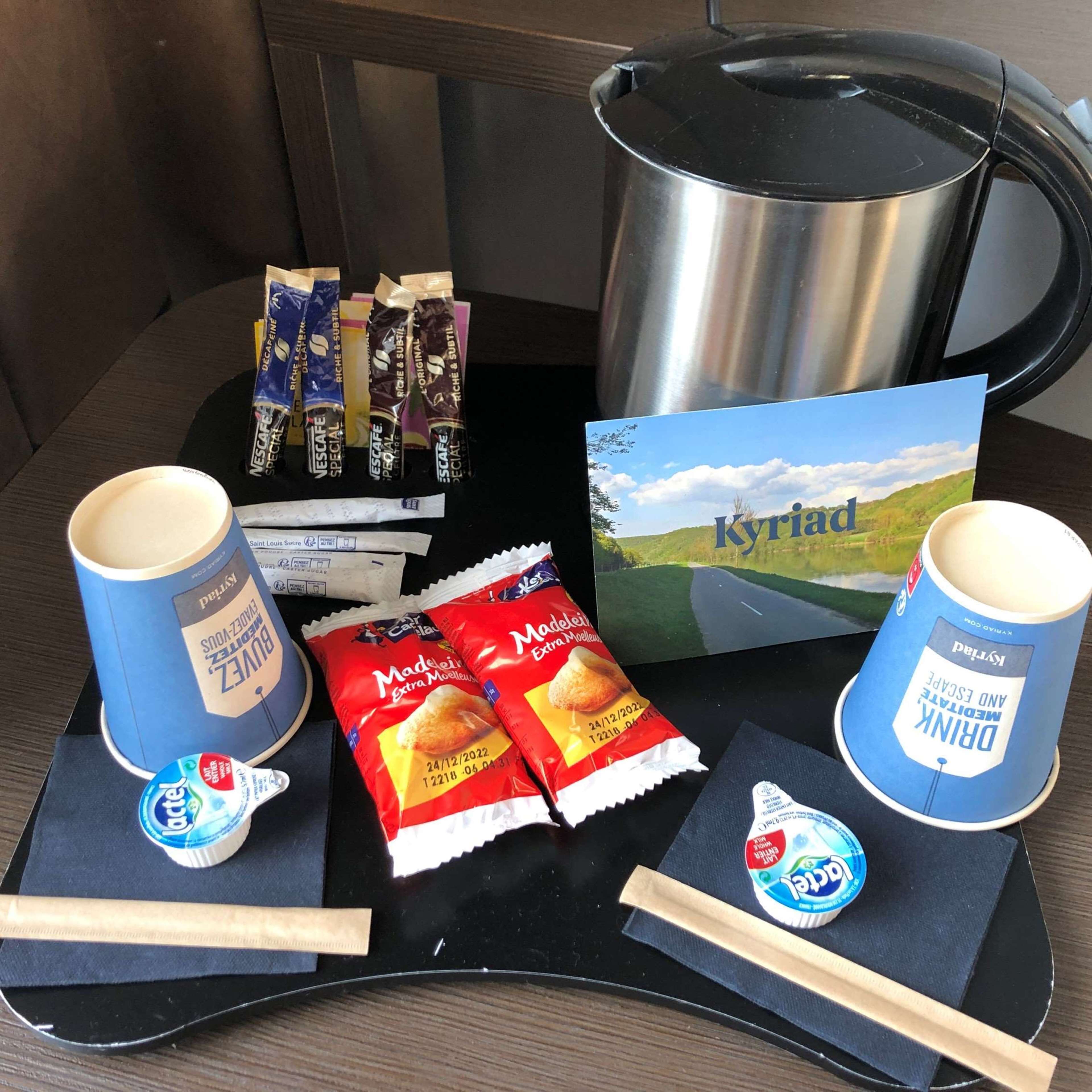 Un tavolo con una macchina del caffè, un bollitore, una brochure turistica e diversi prodotti alimentari.