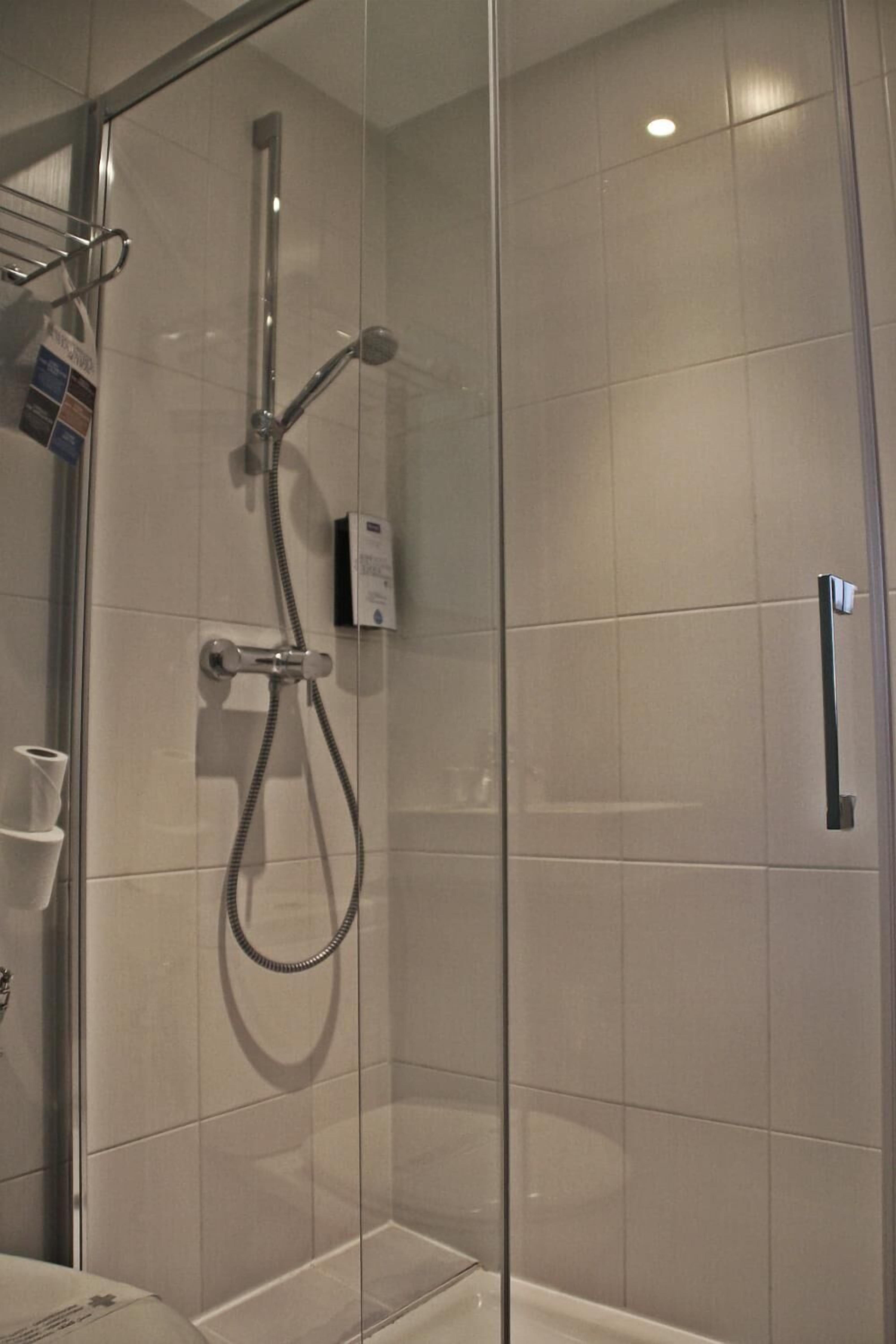 A glass-enclosed shower area with a handheld showerhead and a wall-mounted control panel.