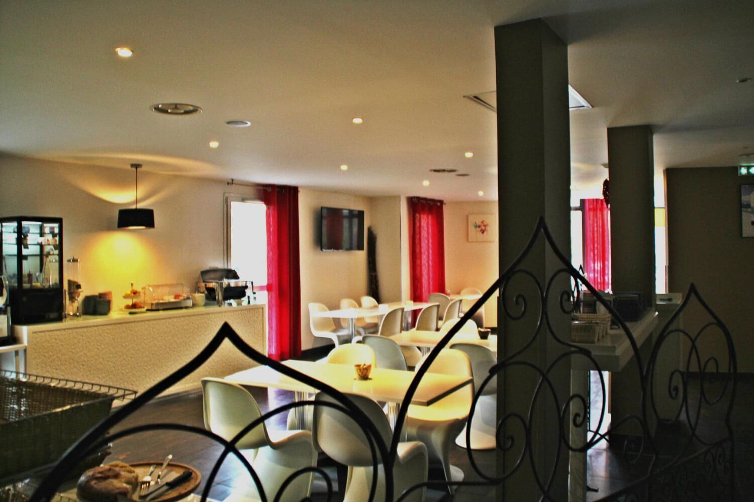 A hotel dining area with tables and chairs, a counter with a cash register, and a television mounted on the wall.