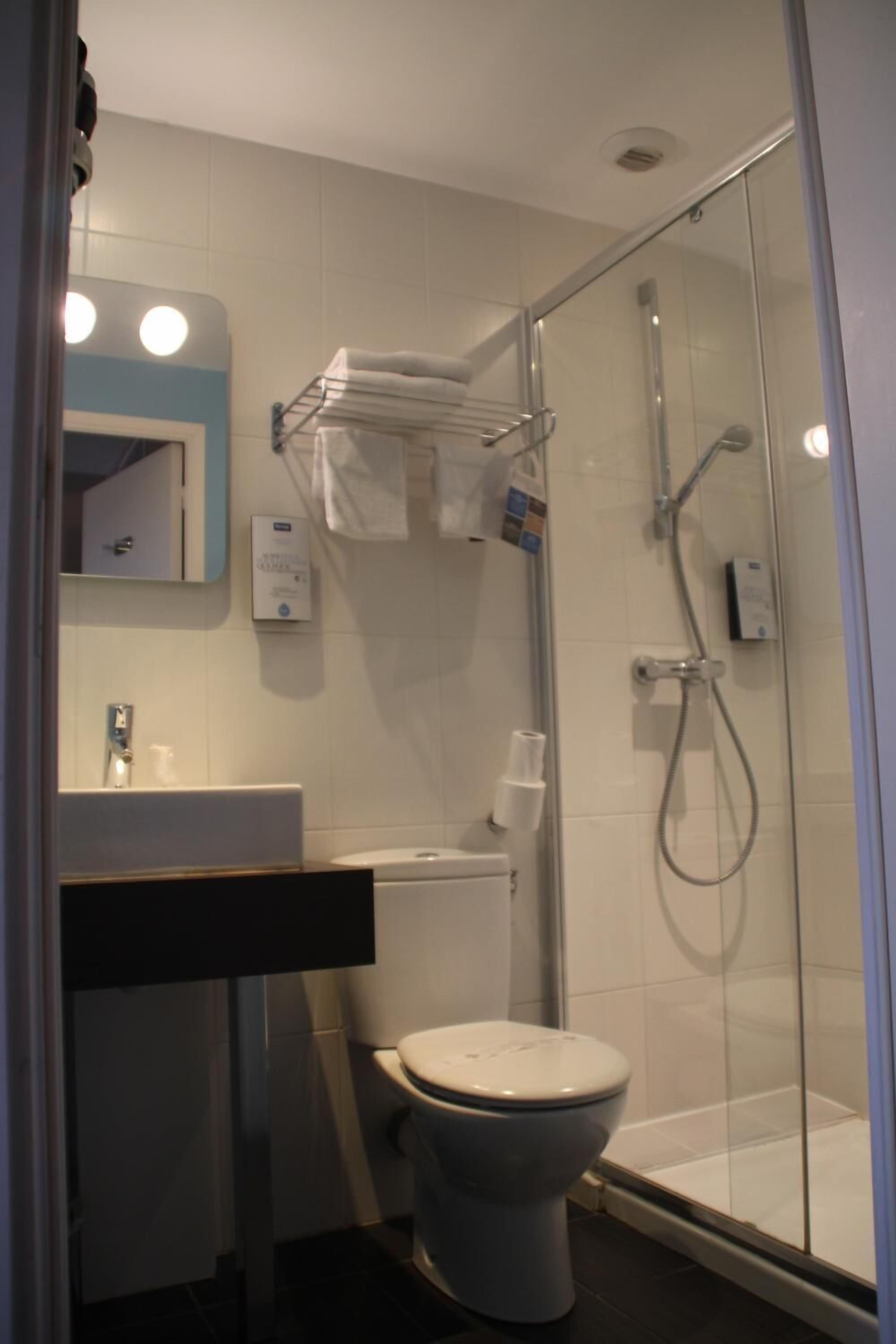 Een moderne badkamer met een douchecabine van glas, een wit toilet, een wastafel met spiegel en een handdoekrek.