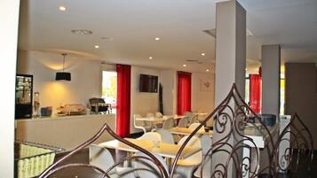 Un restaurante con mesas y sillas blancas, cortinas rojas y una zona de bufé.