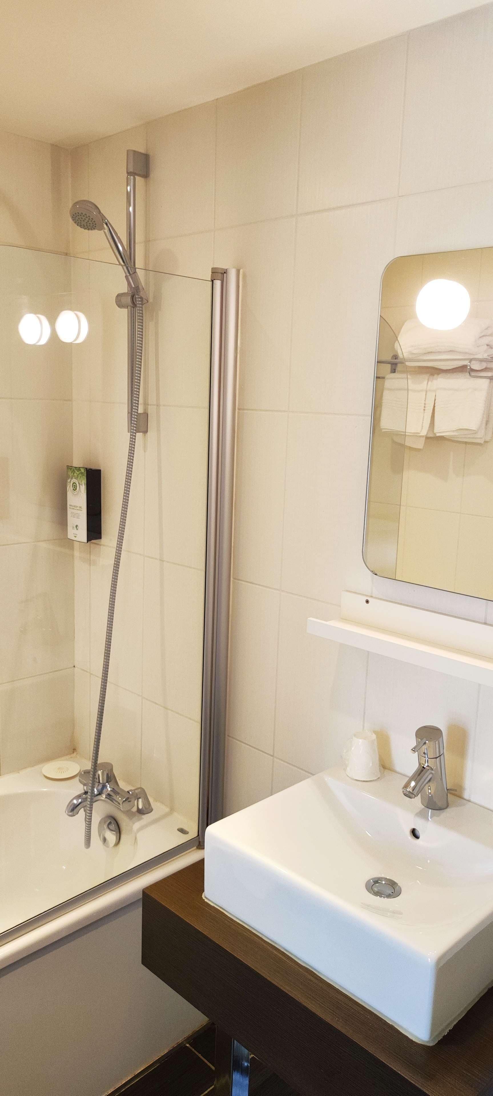 Een moderne badkamer met een douchecabine van glas, een witte wastafel en een spiegel erboven.