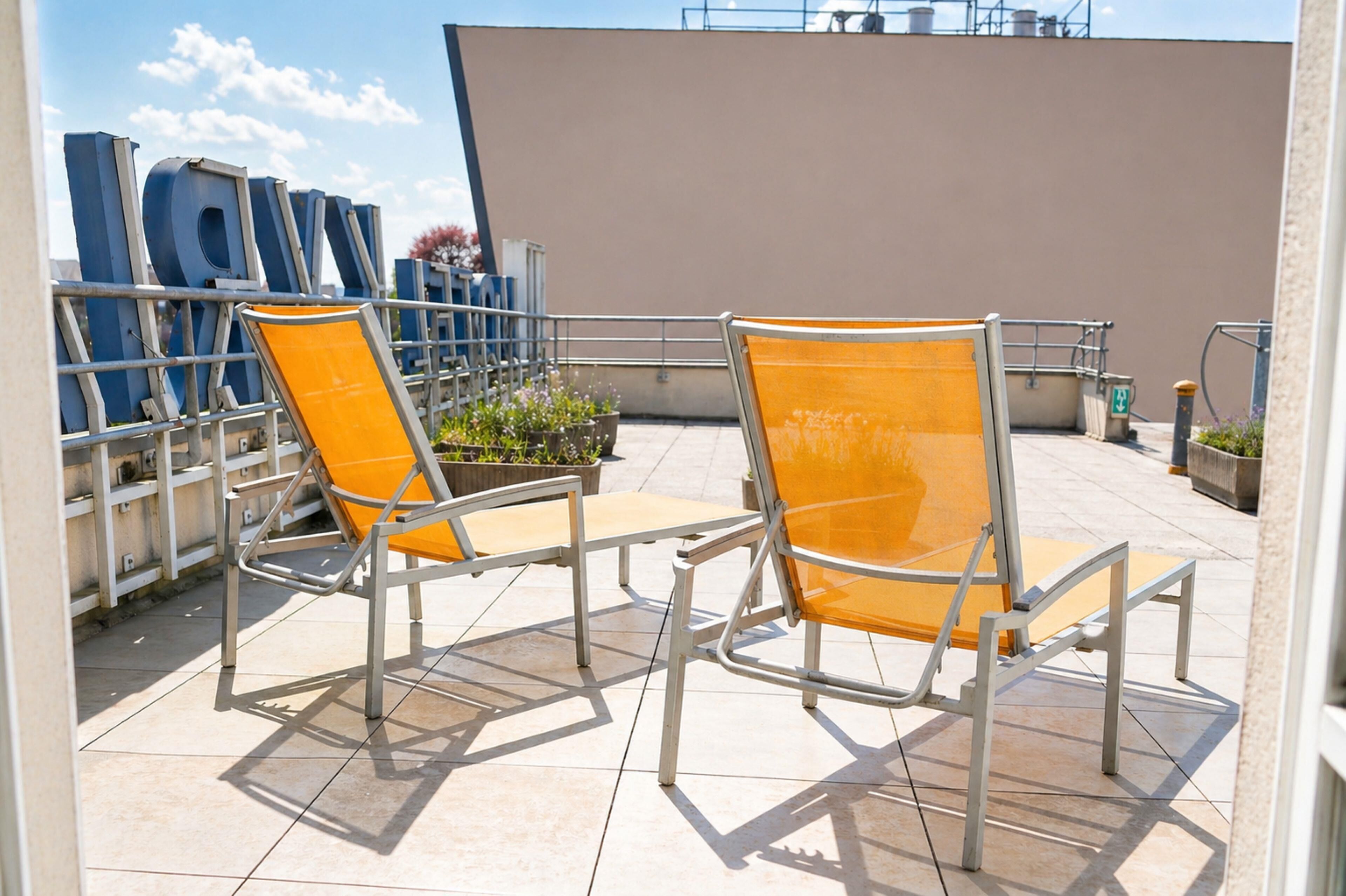 Una terraza en la azotea con dos sillas amarillas, una baranda de metal y una pared grande color beige.