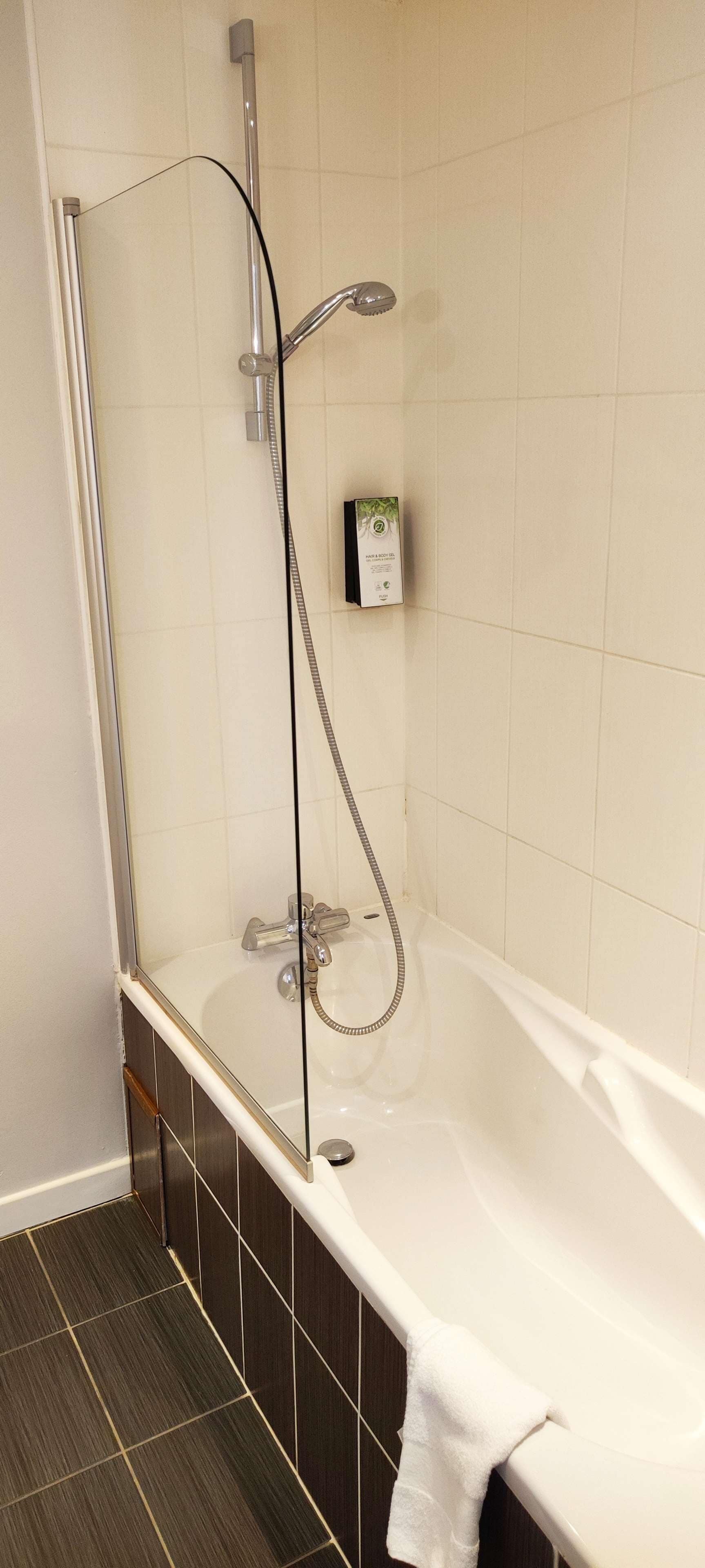 Un baño moderno con ducha de vidrio, una bañera blanca y un estante pequeño con una caja.