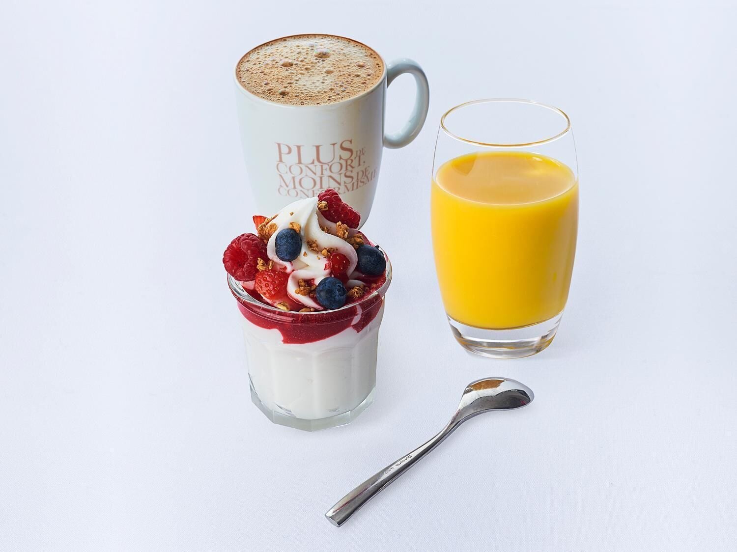 A breakfast setting with a cup of coffee, a glass of orange juice, and a yogurt parfait with berries and granola.