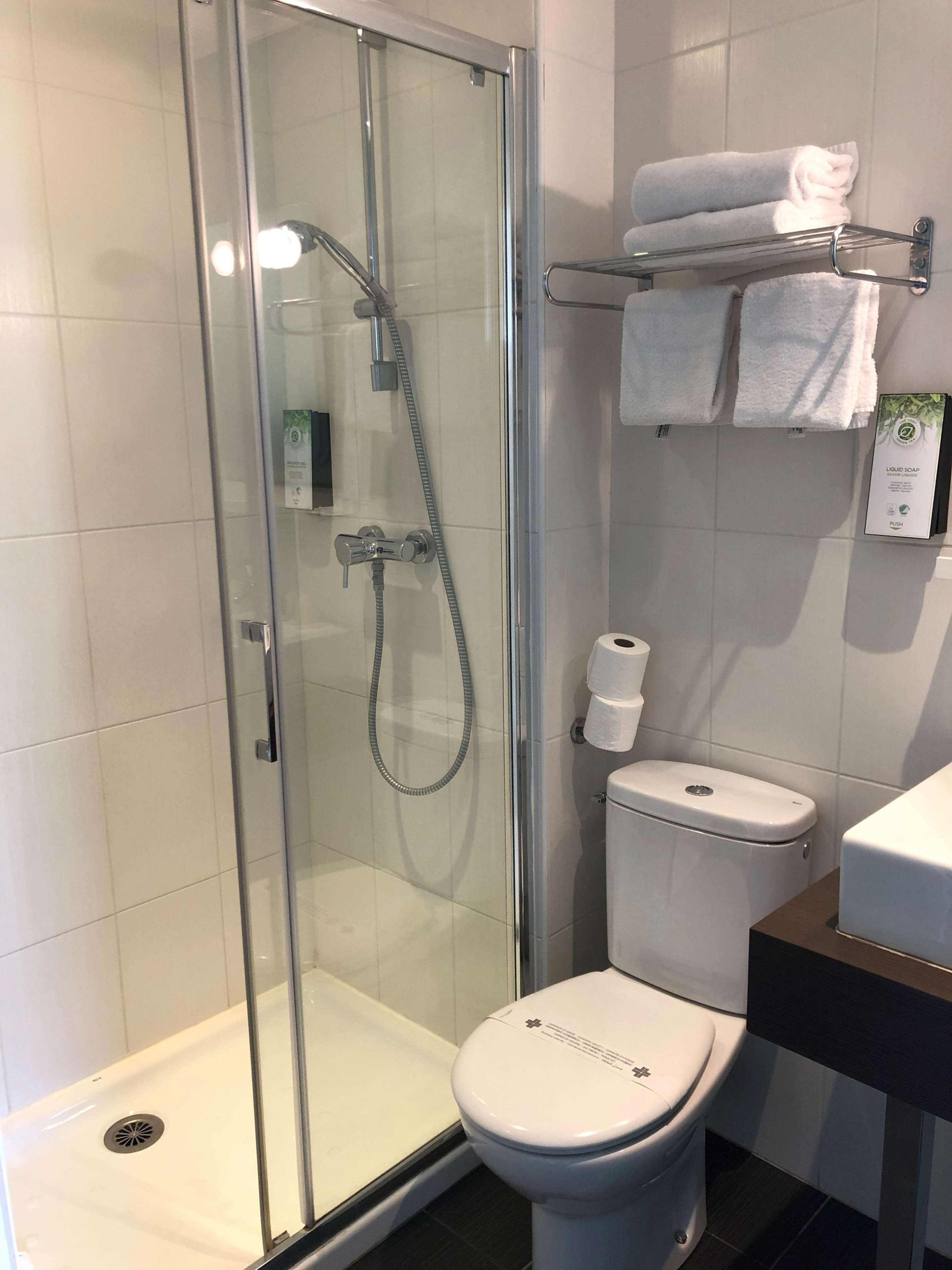 Un baño moderno con ducha de vidrio, inodoro blanco y estante con toallas.