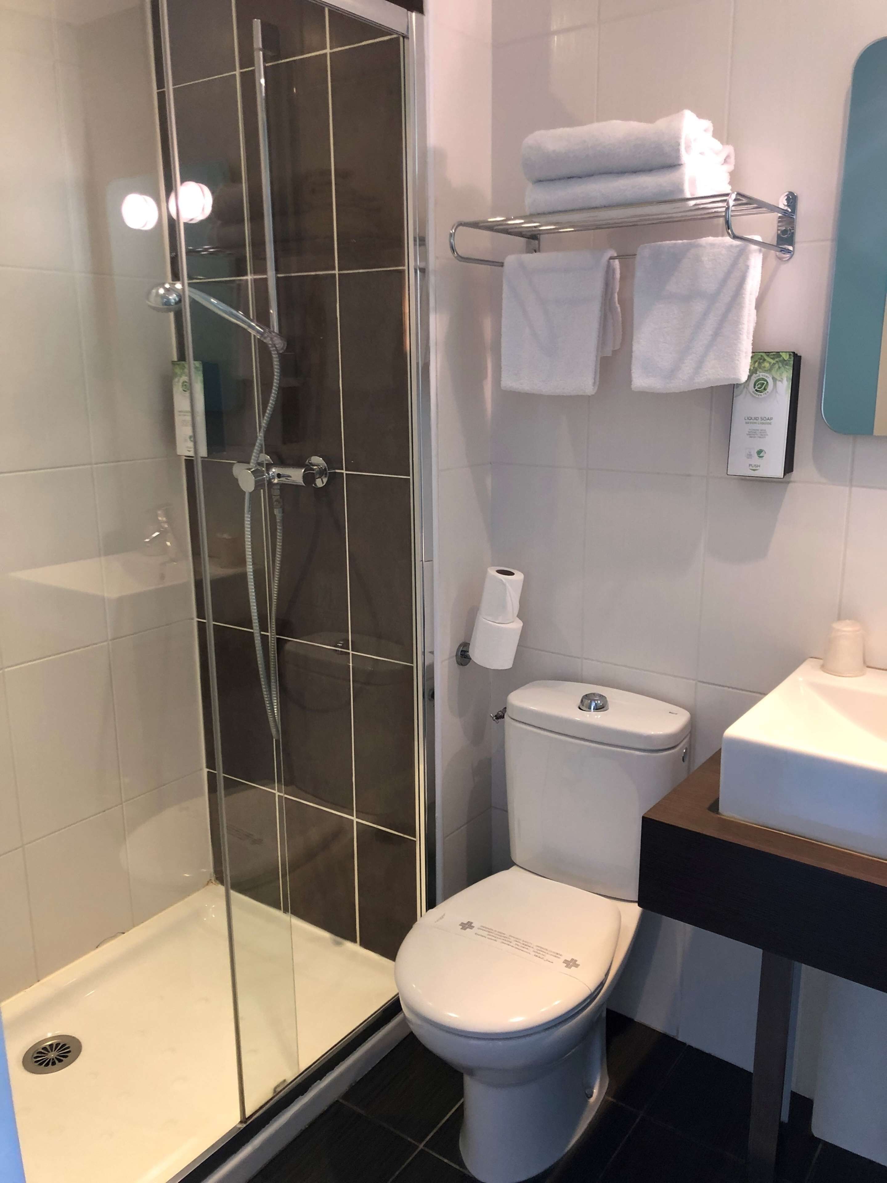 A modern bathroom with a glass-enclosed shower, a toilet, and a sink with a towel rack above it.