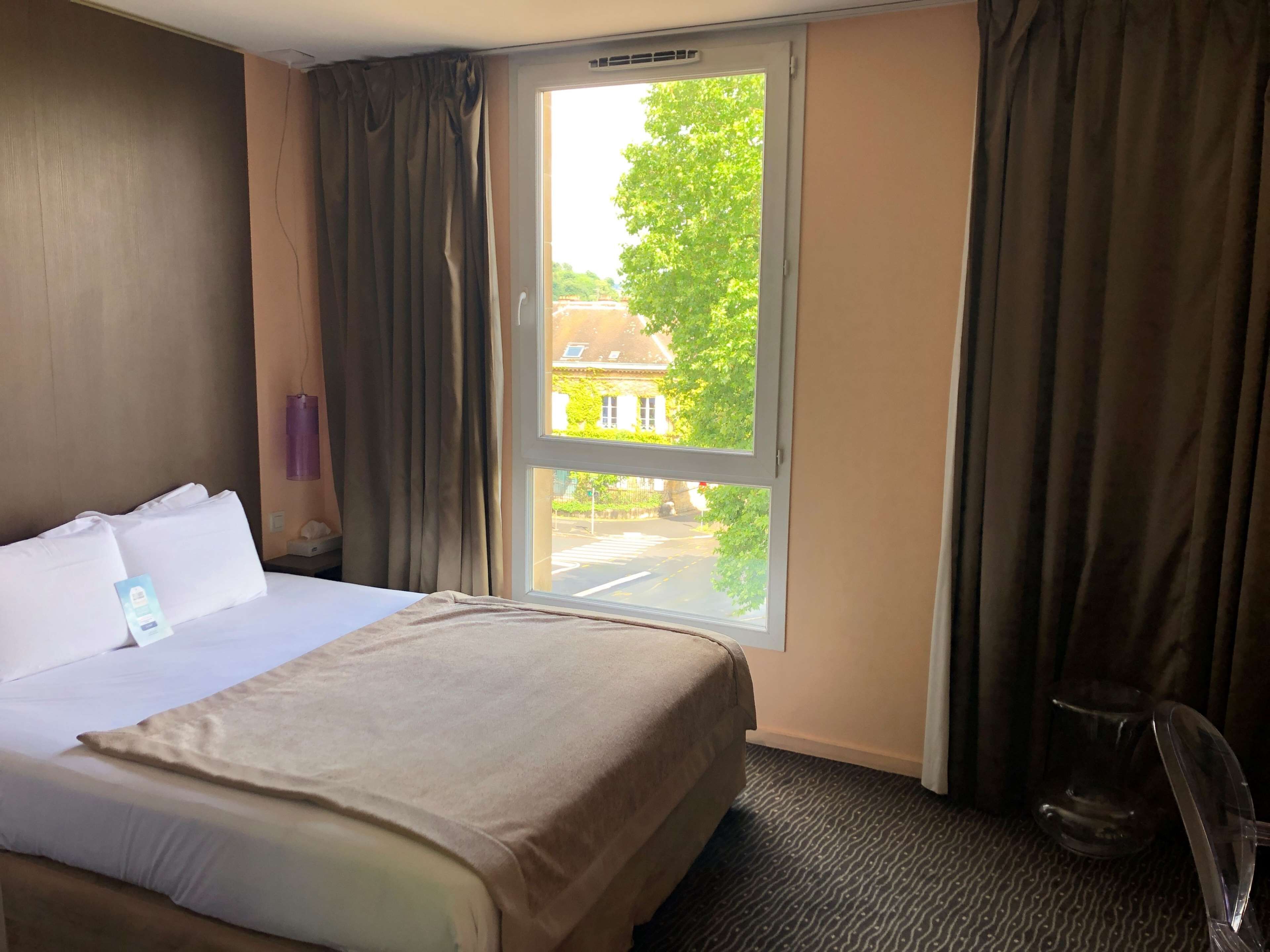 A hotel room with a bed, a window, and a chair.