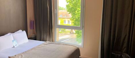 A hotel room with a bed, a window, and a chair.
