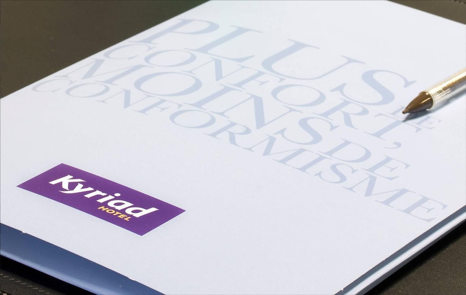 A brochure or booklet with the title "PLUS CONFORT, MOINSSE CONFORMISME" and the logo "Kyriad Hotel" on a white background.
