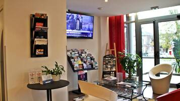 En modern inredning med en receptionsdisk, en tv-skärm, ett glasbord och sittgrupper.