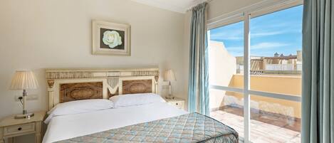 Un cuarto de hotel con una cama grande, una mesita de noche, una lámpara, un cuadro en la pared y vista a la ciudad por la ventana.