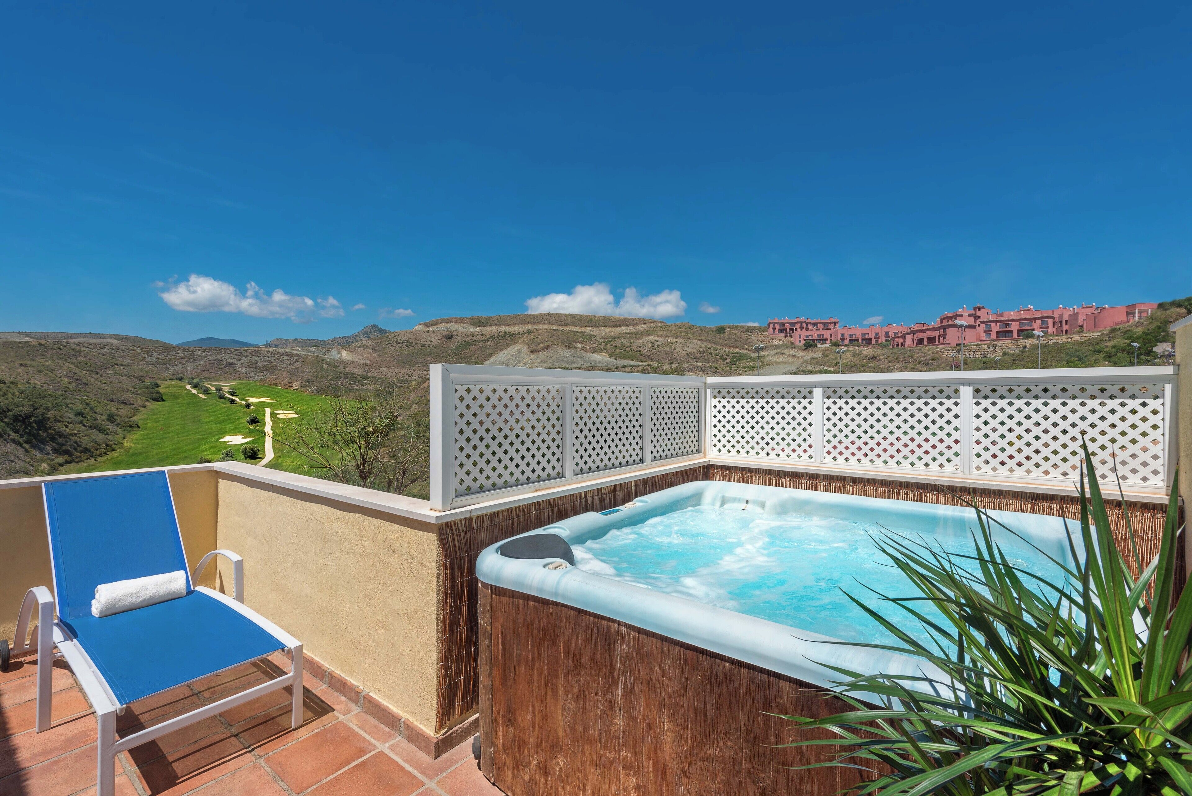 A hot tub on a balcony with a view of a golf course and buildings in the distance.