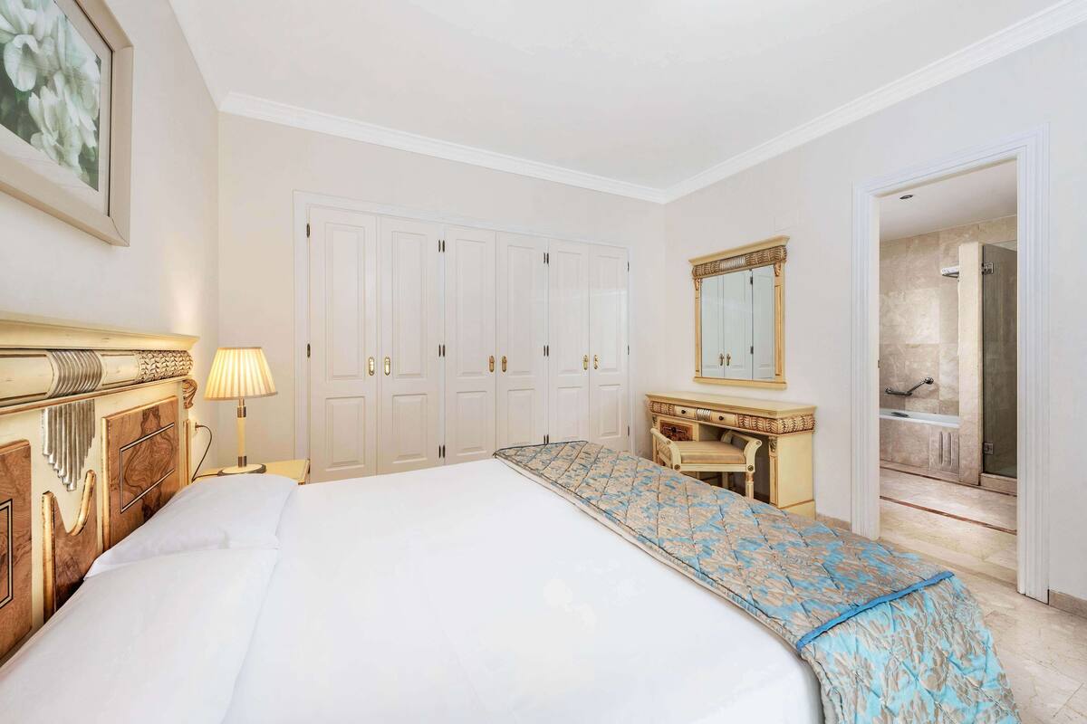 Ein Hotelzimmer mit einem großen Bett, einem Holzschrank, einem Spiegel und einer Tür zu einem Badezimmer.