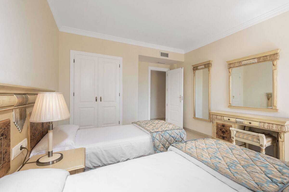 Ein Hotelzimmer mit zwei Betten, einem Schreibtisch, einer Lampe, einem Schminktisch und einem Spiegel.