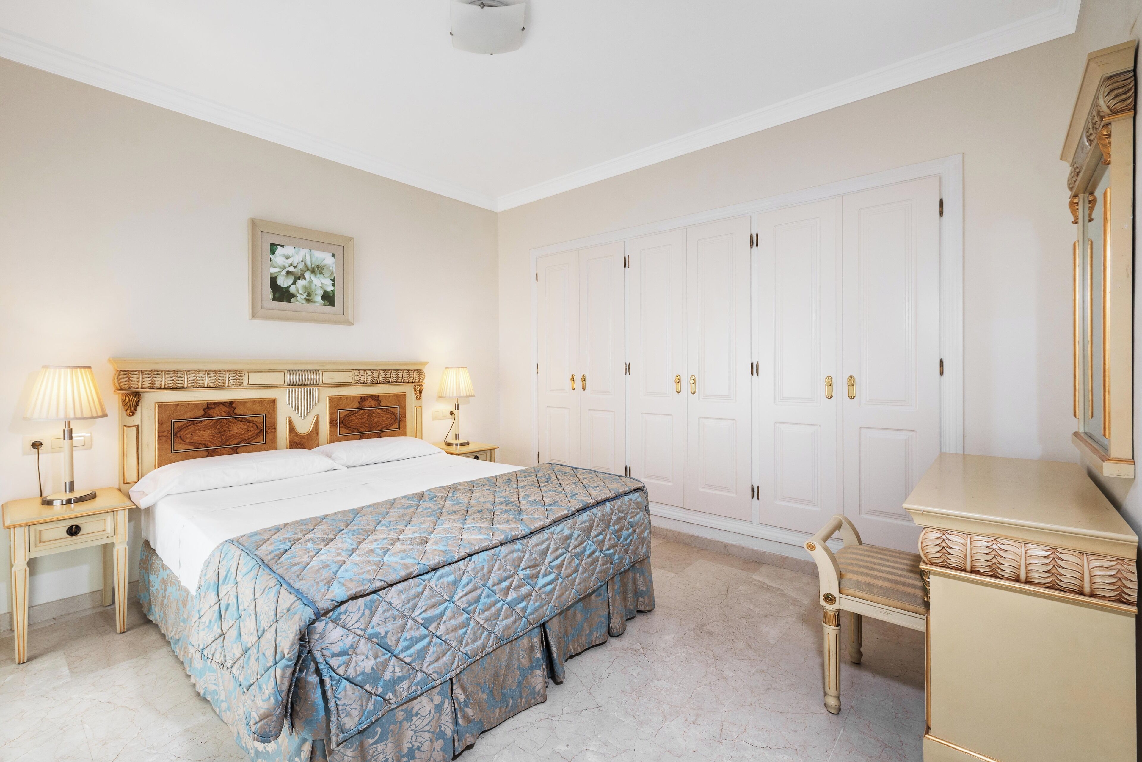 Une chambre à coucher avec un grand lit, deux tables de chevet avec des lampes, une commode et une armoire à plusieurs portes.