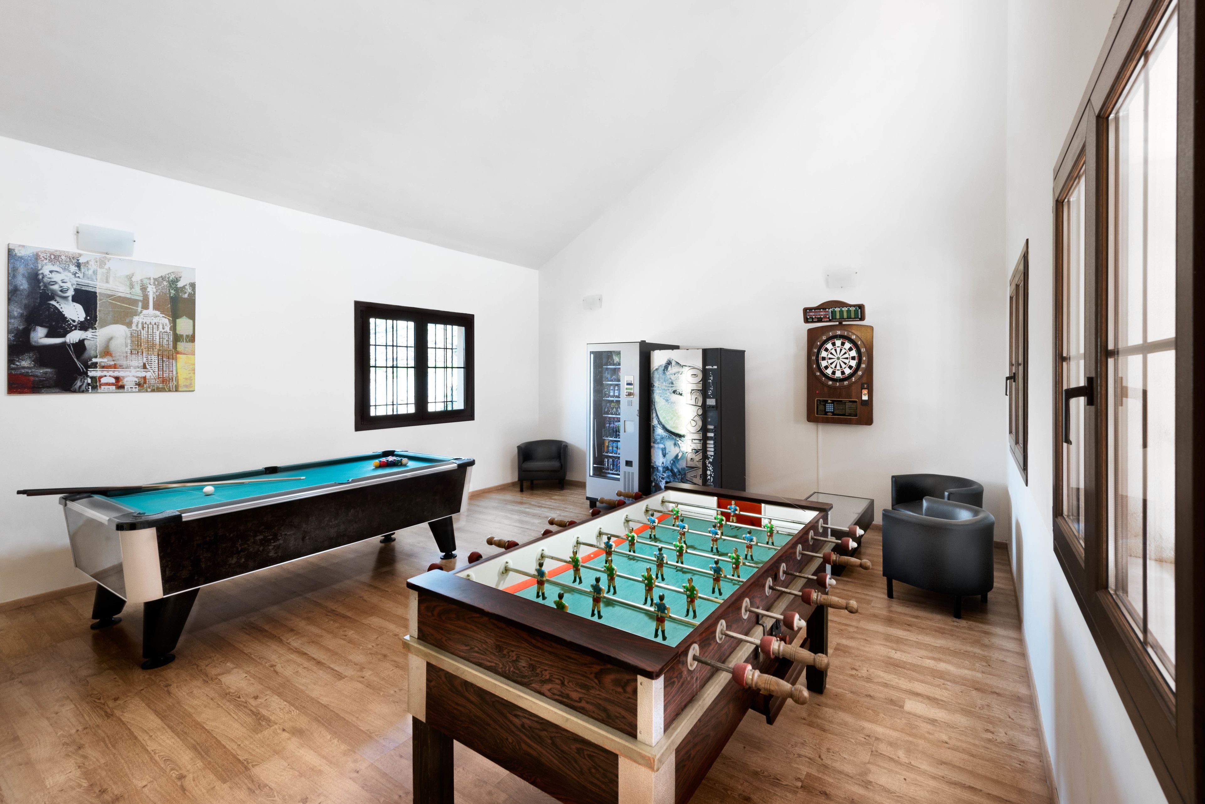 A room with a foosball table, a pool table, and a dartboard.