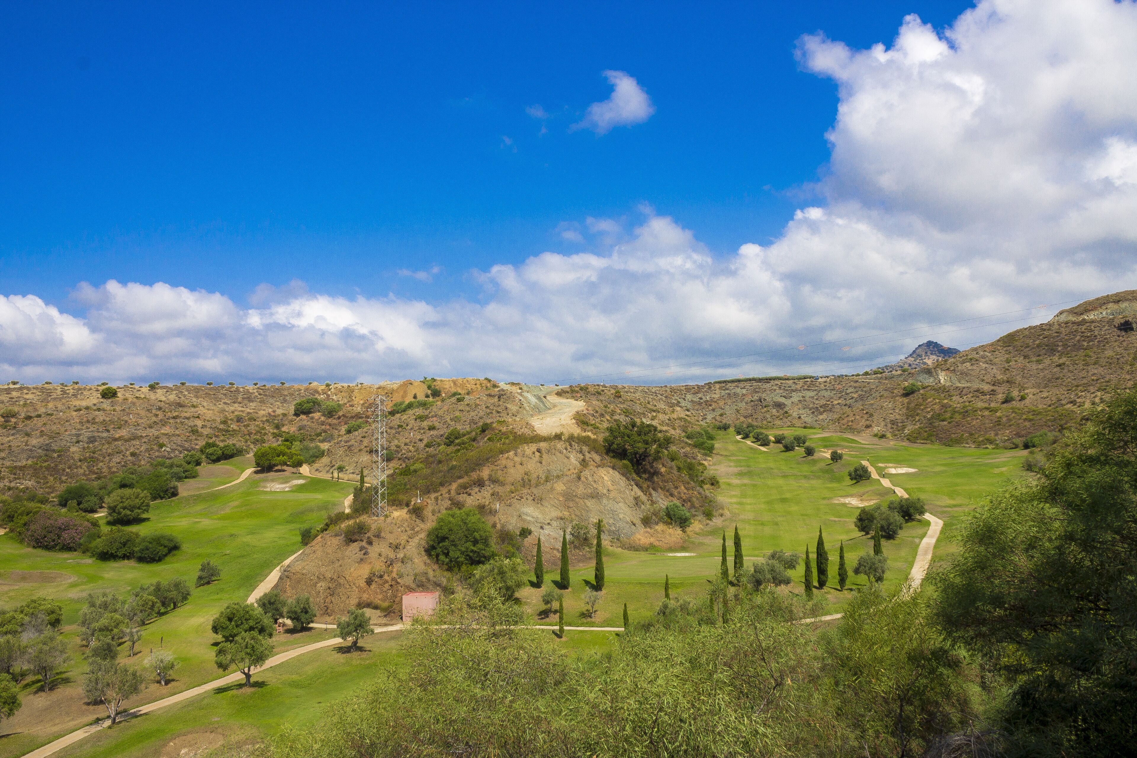 A golf course with a clear sky, rolling hills, and sparse vegetation.