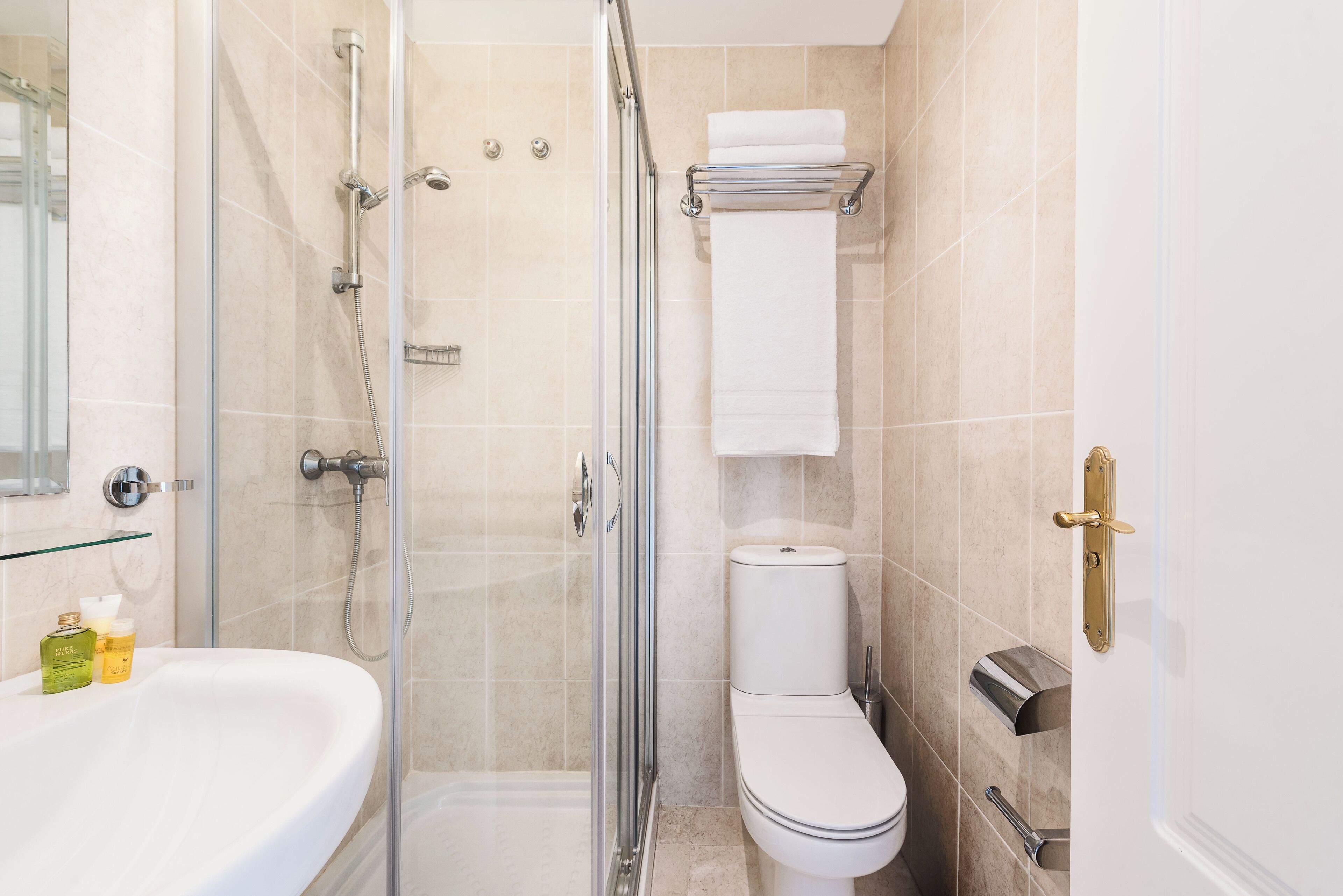 Un baño moderno con ducha de vidrio, un lavamanos blanco con artículos de aseo, un inodoro y un perchero para toallas.