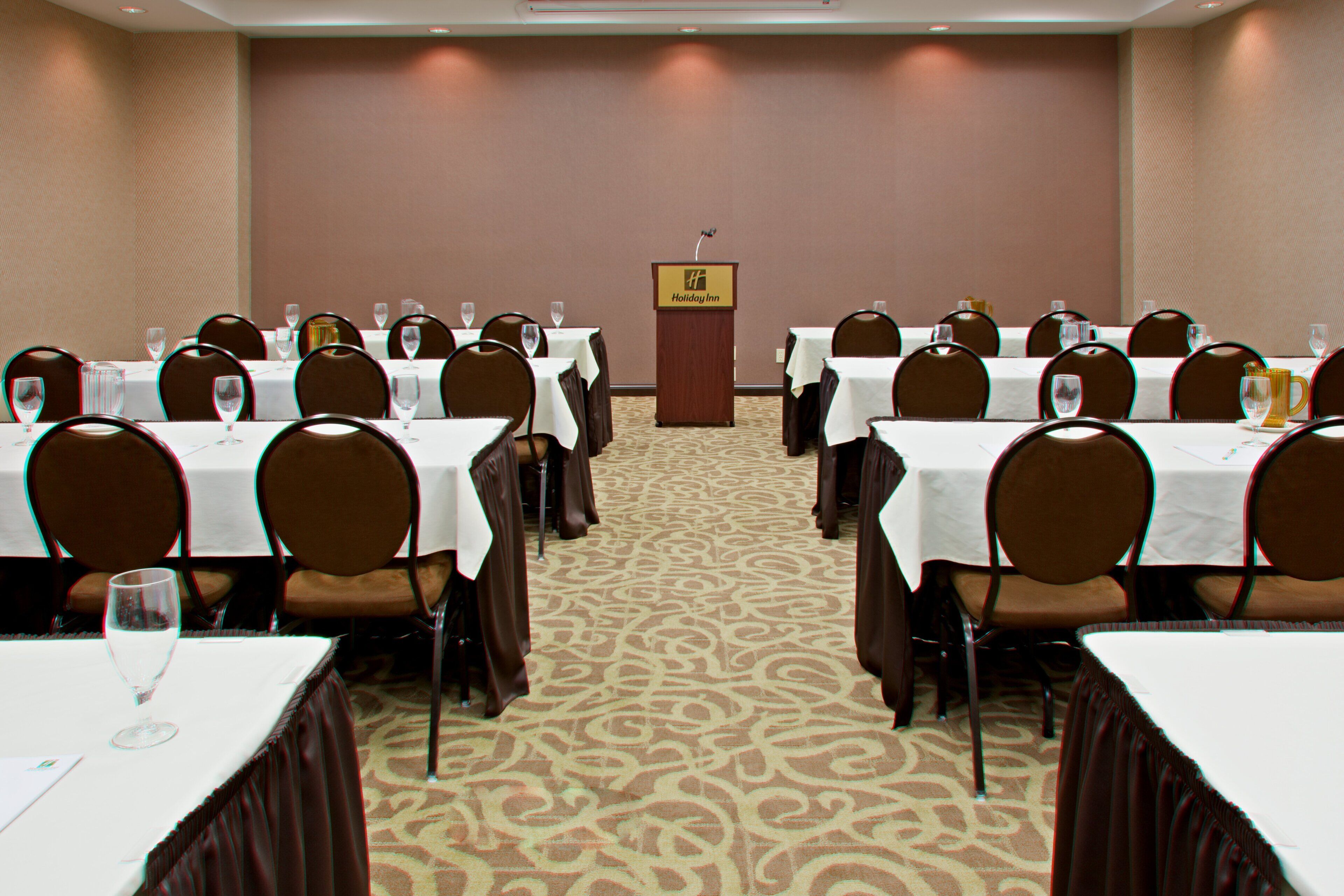 A conference room with tables set for a meeting, a podium, and a carpeted floor.