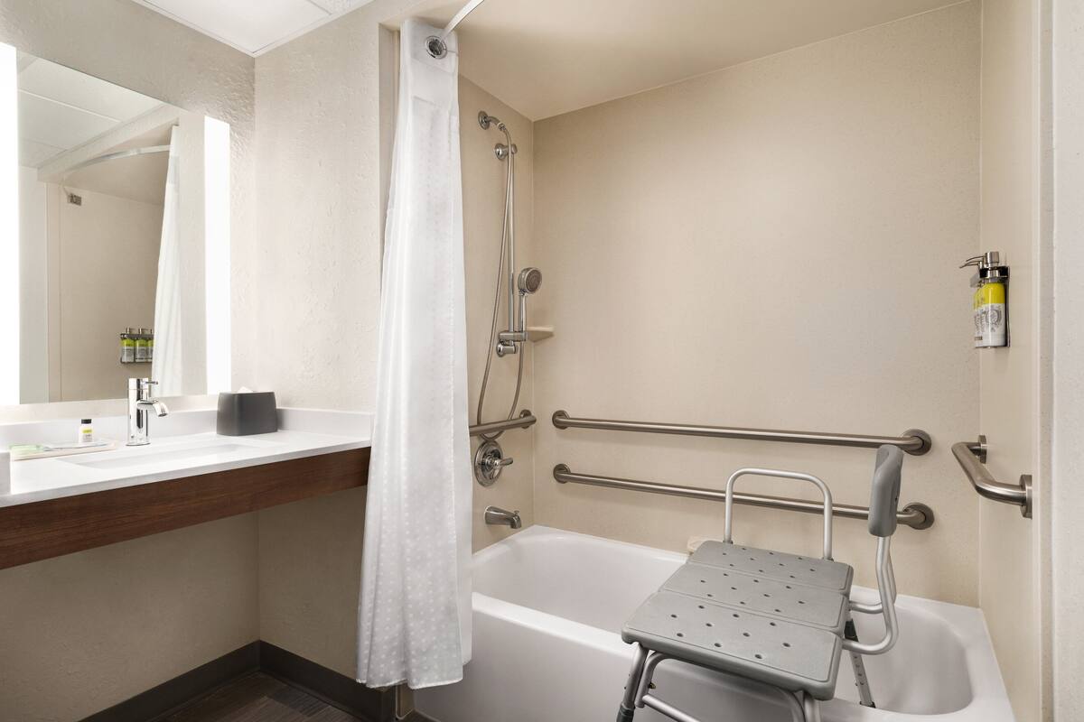 A bathroom with a bathtub, a shower, a handrail, and a grab bar.