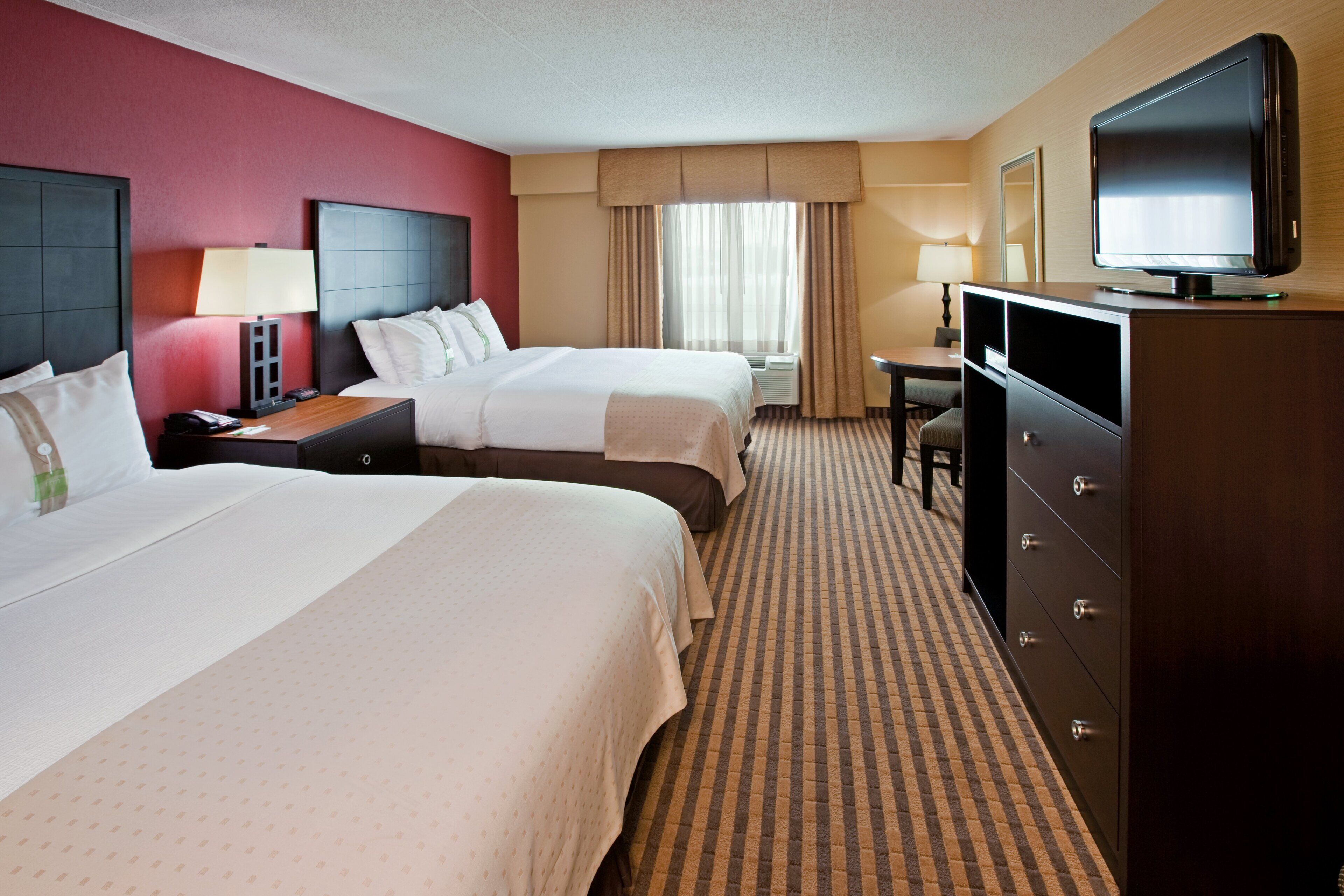 A hotel room with two beds, a television, a desk, and a dresser.