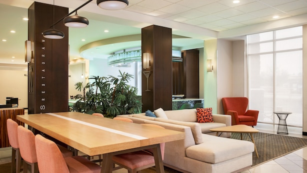 A modern hotel lobby with a long wooden table, several cushioned chairs, a sofa, a red armchair, and a small side table. - Holiday Inn Florence by IHG (Florence)