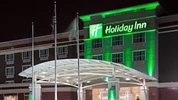 Un hotel Holiday Inn con un llamativo letrero verde, una entrada cubierta y un asta con la bandera estadounidense.