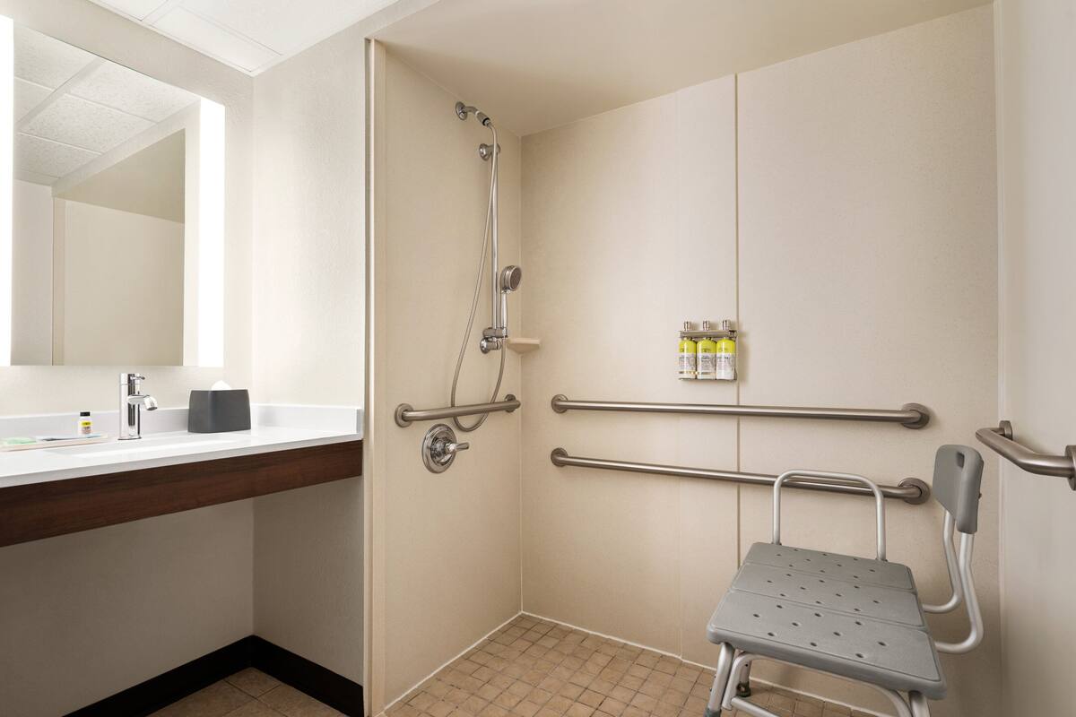 A bathroom with a shower, grab bars, a sink, and a mirror.