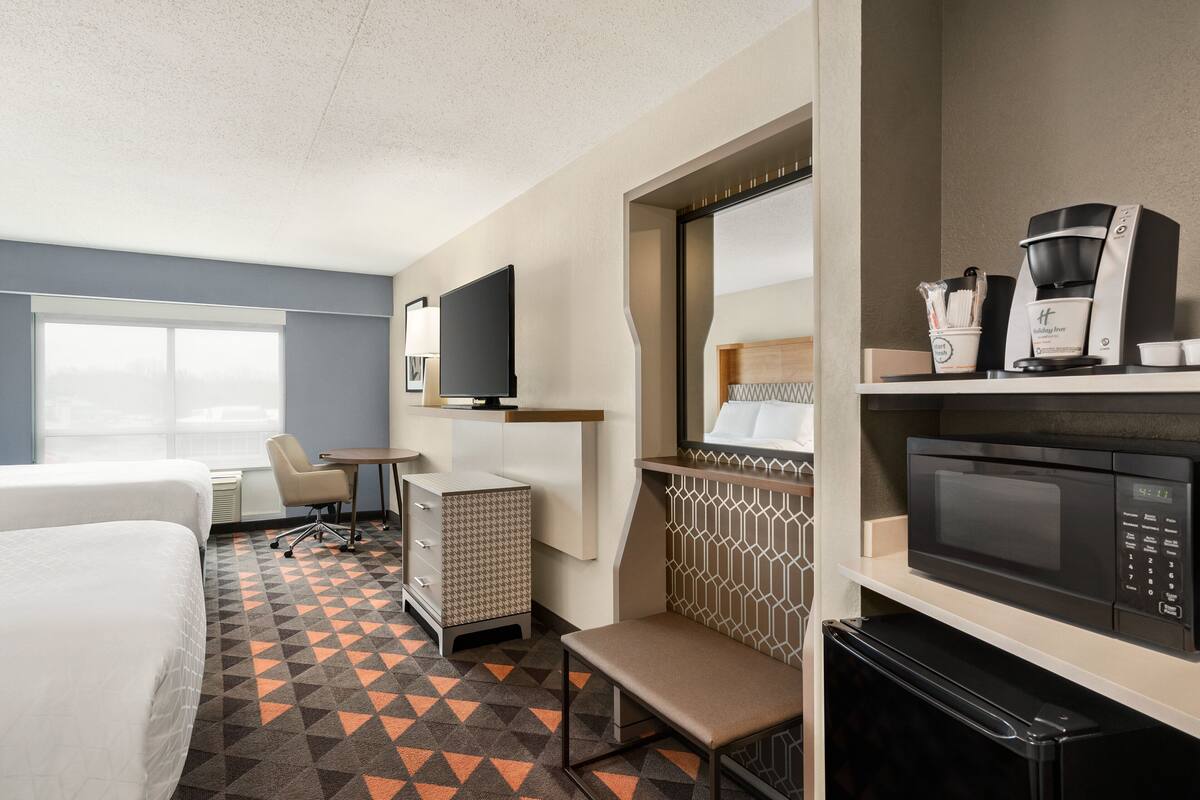 A hotel room with a bed, a desk, a chair, a television, a microwave, and a coffee machine.