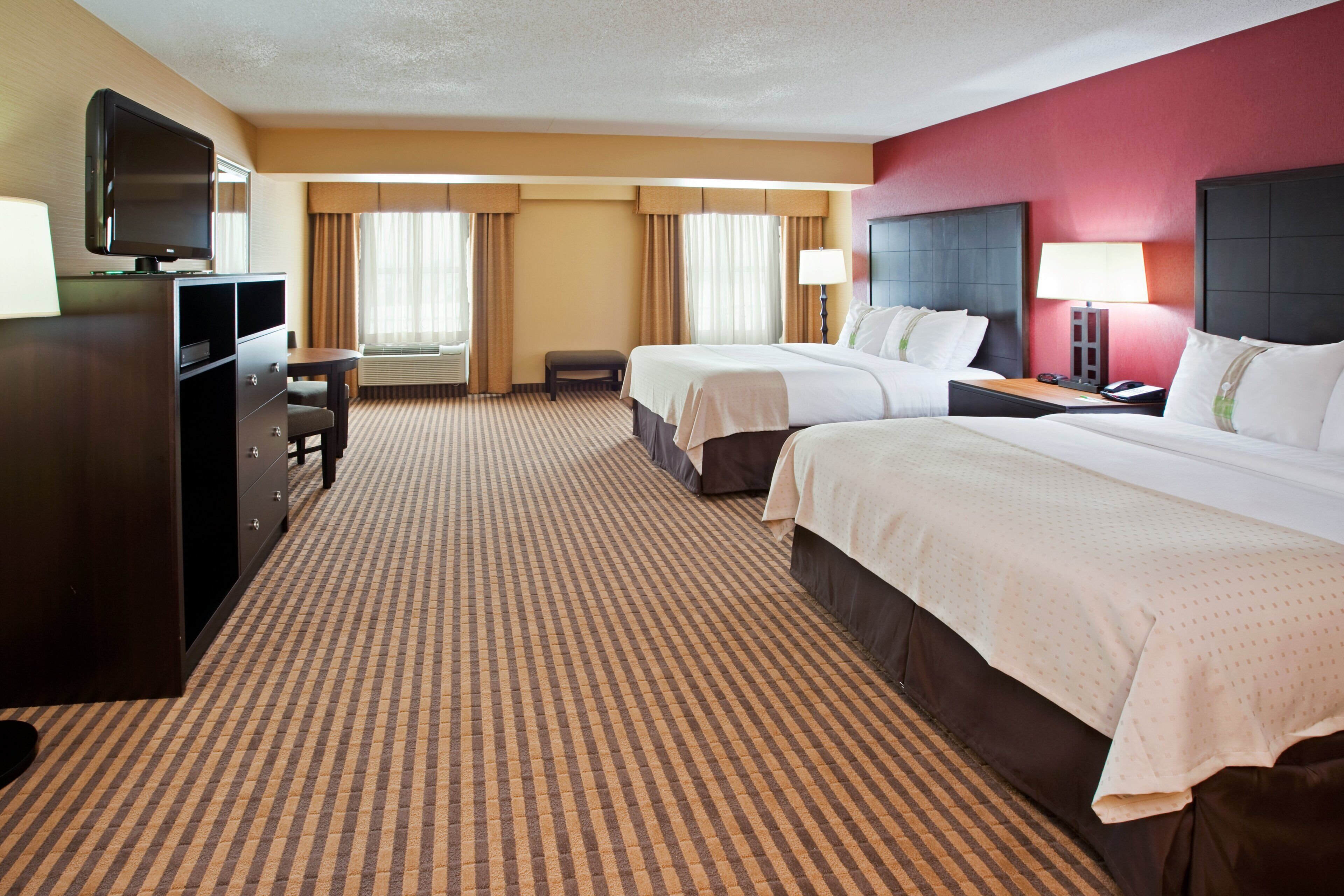 A hotel room with two beds, a desk, a television, and a window with curtains.