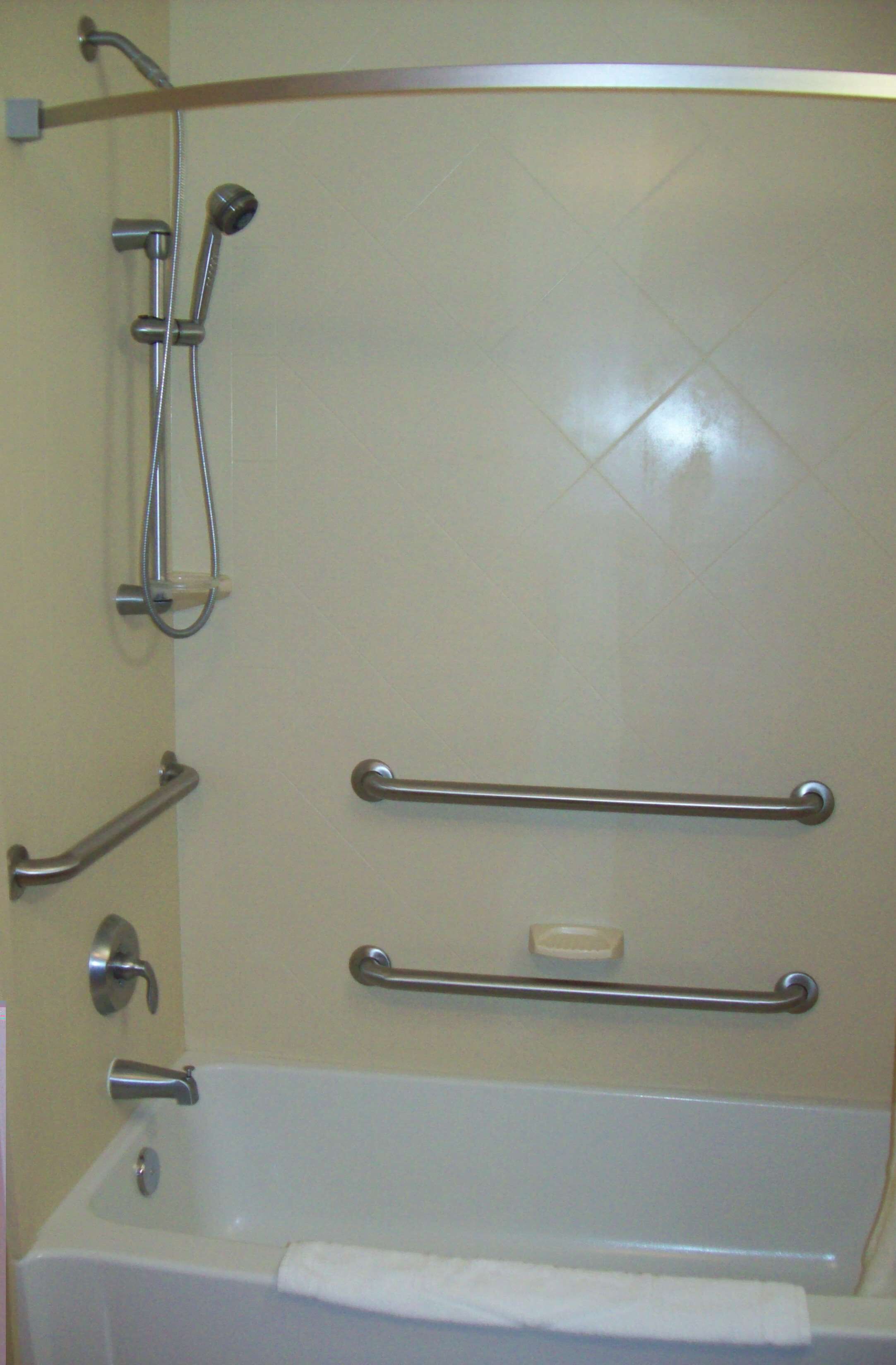 A bathroom with a bathtub, grab bars, a showerhead, and a soap dish.