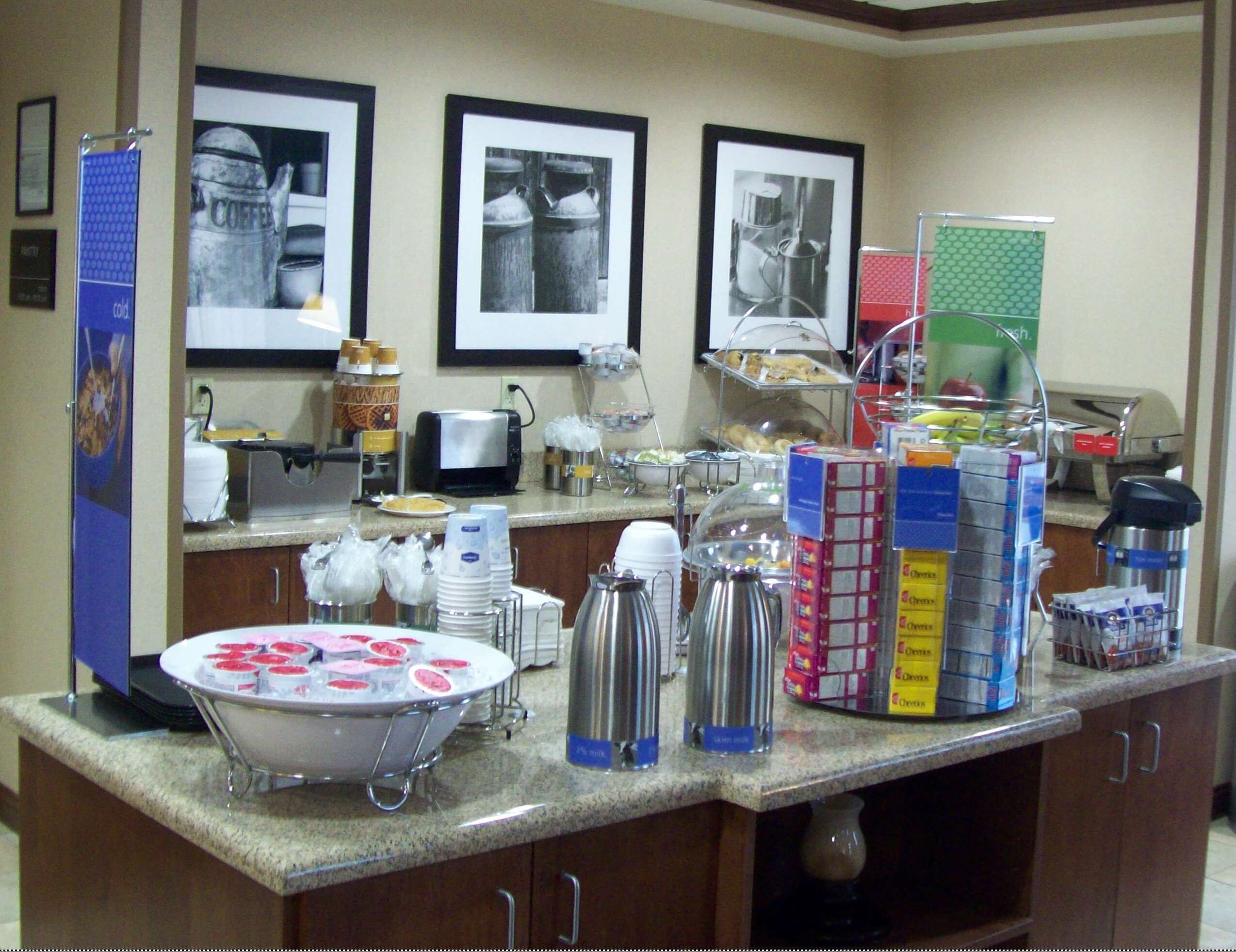 A hotel breakfast area with a buffet setup, including various food items, condiments, and a coffee station.