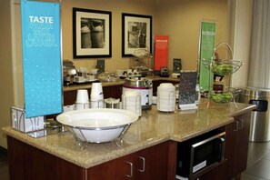 A hotel breakfast area with a buffet setup, including a large bowl, coffee makers, and a sign that reads "TASTE POUR MIX LAYER LAUGH."