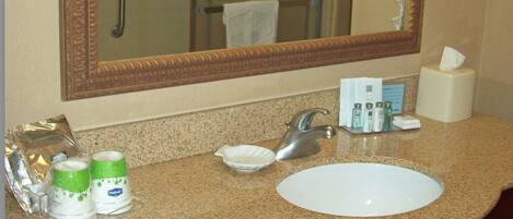 A bathroom with a granite countertop, a white sink, a large mirror, and toiletries.