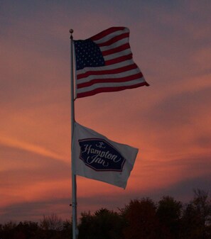 An American flag and a Hampton Inn sign on a flagpole against a sunset sky.