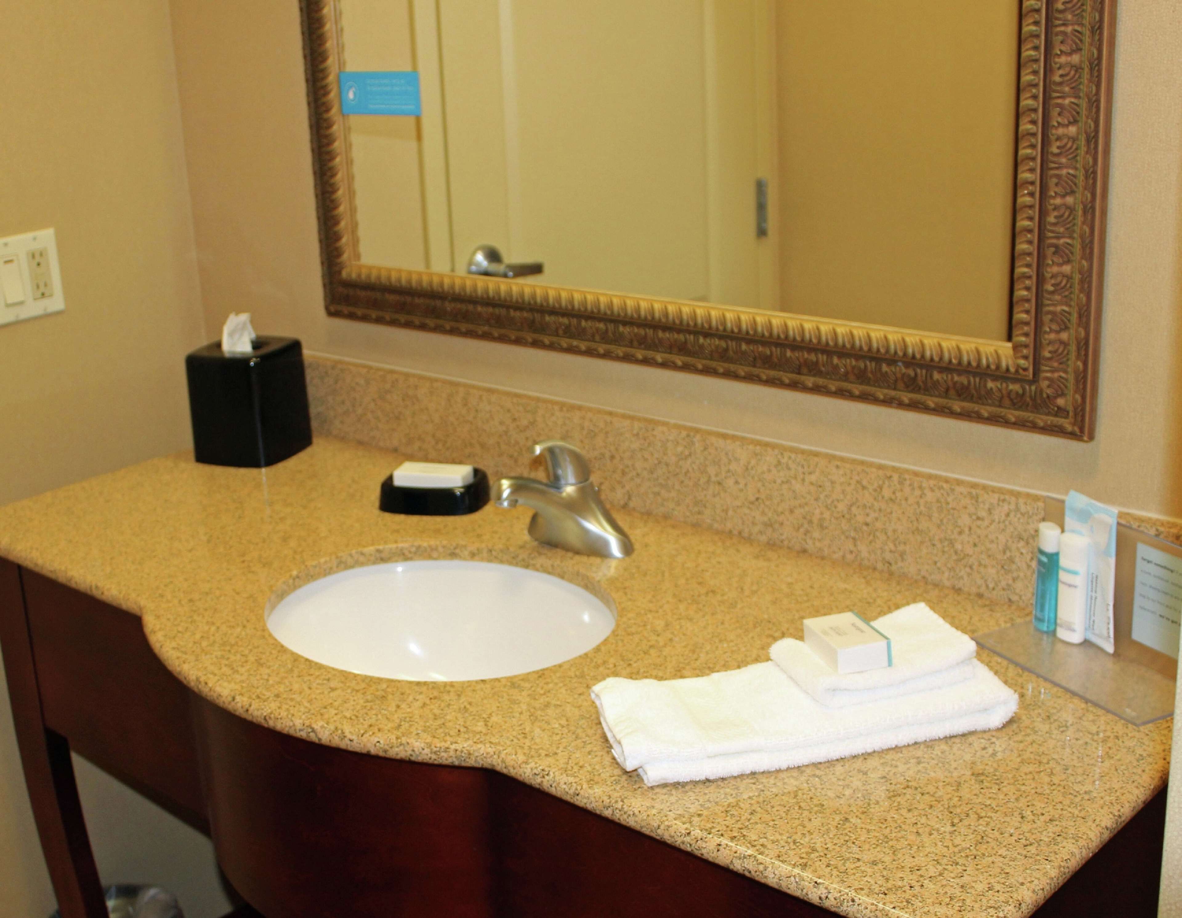 A bathroom with a granite countertop, a white sink, a mirror with an ornate frame, a towel rack, and toiletries.