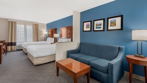 Quarto de hotel com duas camas, um sofá azul, uma mesa de centro de madeira e três quadros na parede.