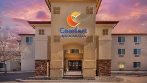 Exterior de um hotel Comfort Inn & Suites, com logotipo em destaque, entrada central e um edifício de vários andares com telhado plano.