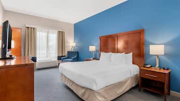 Habitación de hotel con una cama grande, un escritorio con televisor, una silla y una lámpara de escritorio.